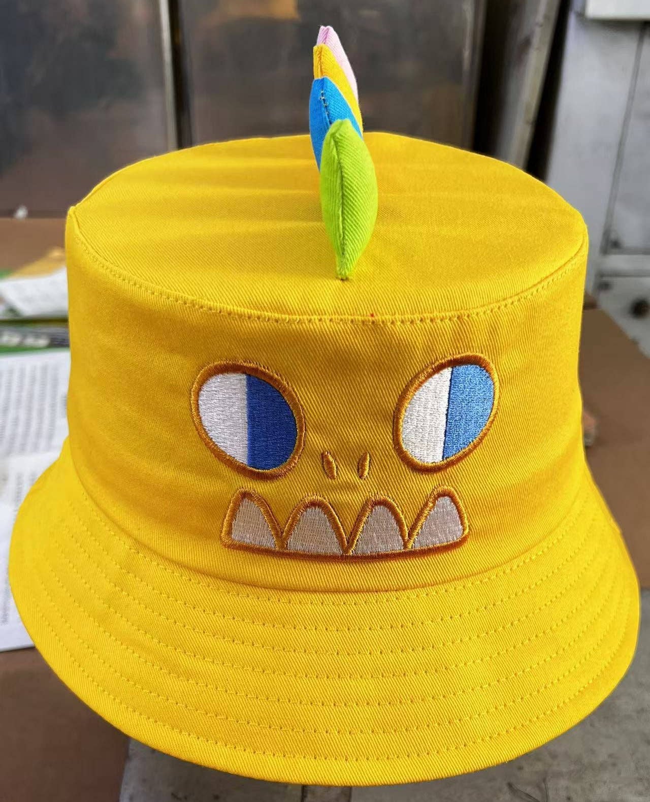 Yellow bucket hat with a cartoon face design on a flat surface.