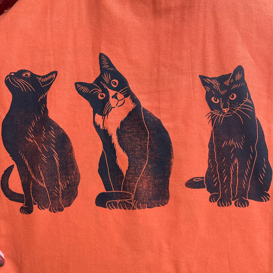 Orange tote bag with black cat illustrations held by a person.