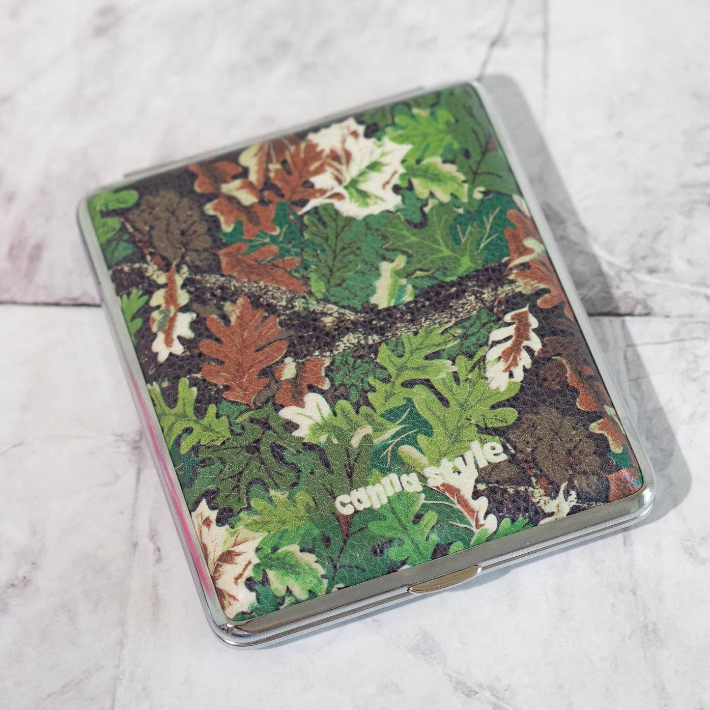 Camouflage-patterned cigarette case with 'Canna Style' branding on a marble surface