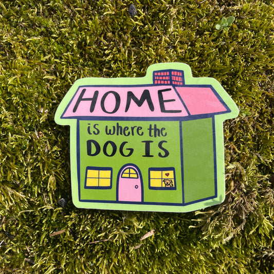Colorful house-shaped sign with 'HOME is where the DOG IS' text on a grass background