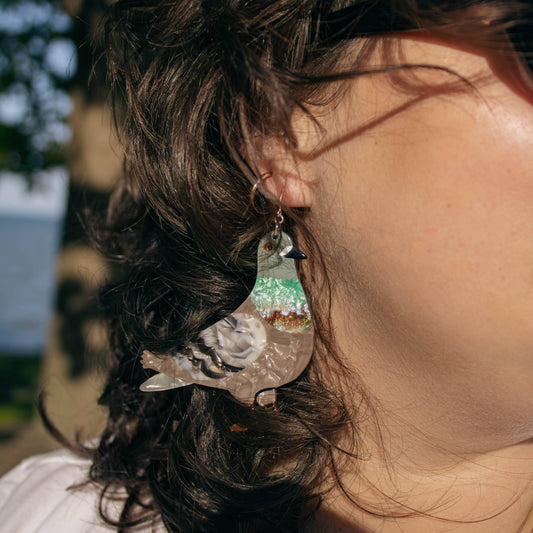 Close-up of a person with styled hair and pigeon earrings outdoors
