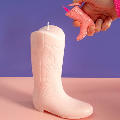 Pink boot-shaped candle with a hand holding a pink cowboy boot lighter against a purple background