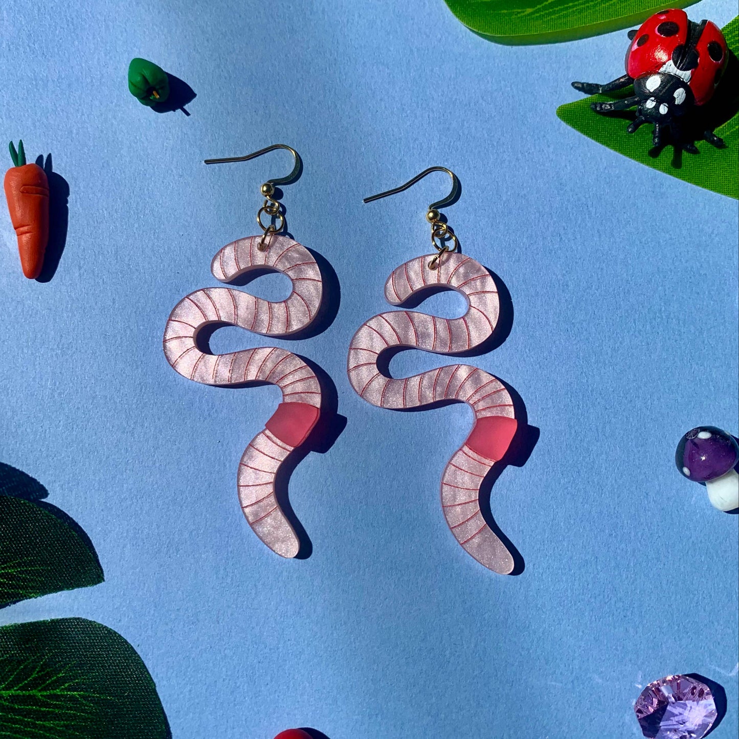 Worm earrings on a blue background with decorative elements.