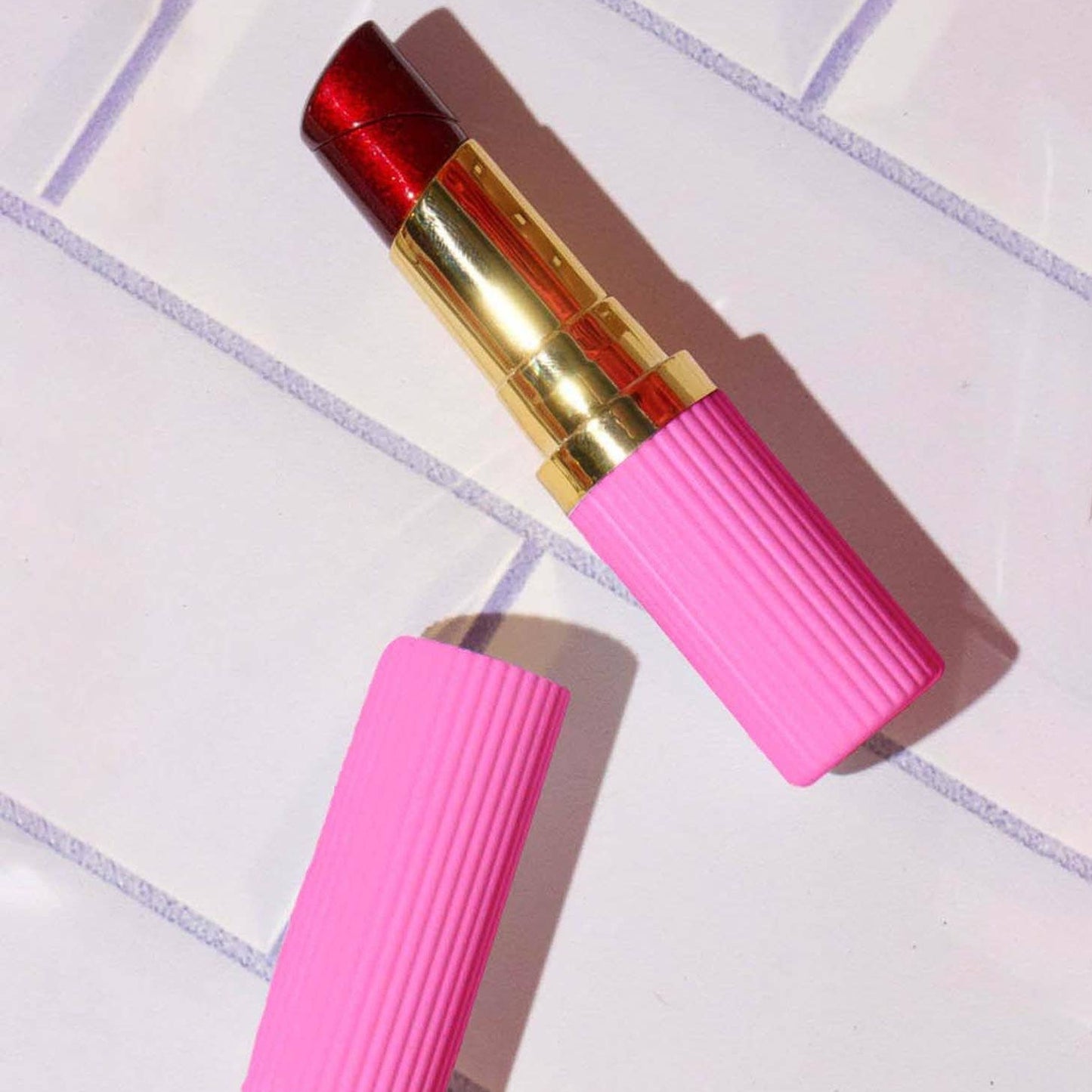 Pink lipstick lighter with gold cap on a tiled surface