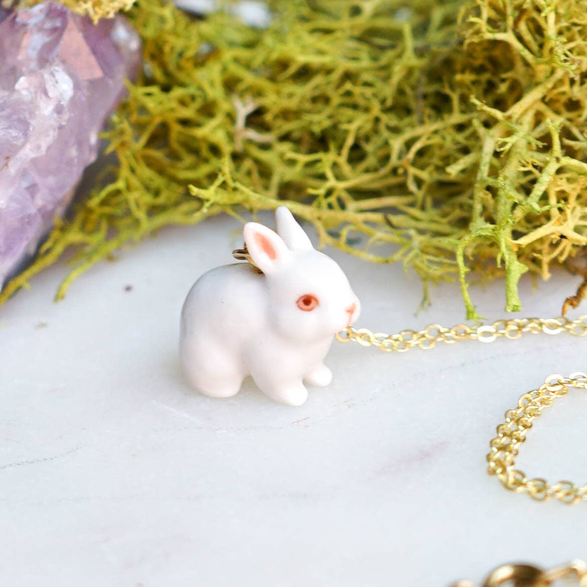 White rabbit pendant on a gold chain with a natural background