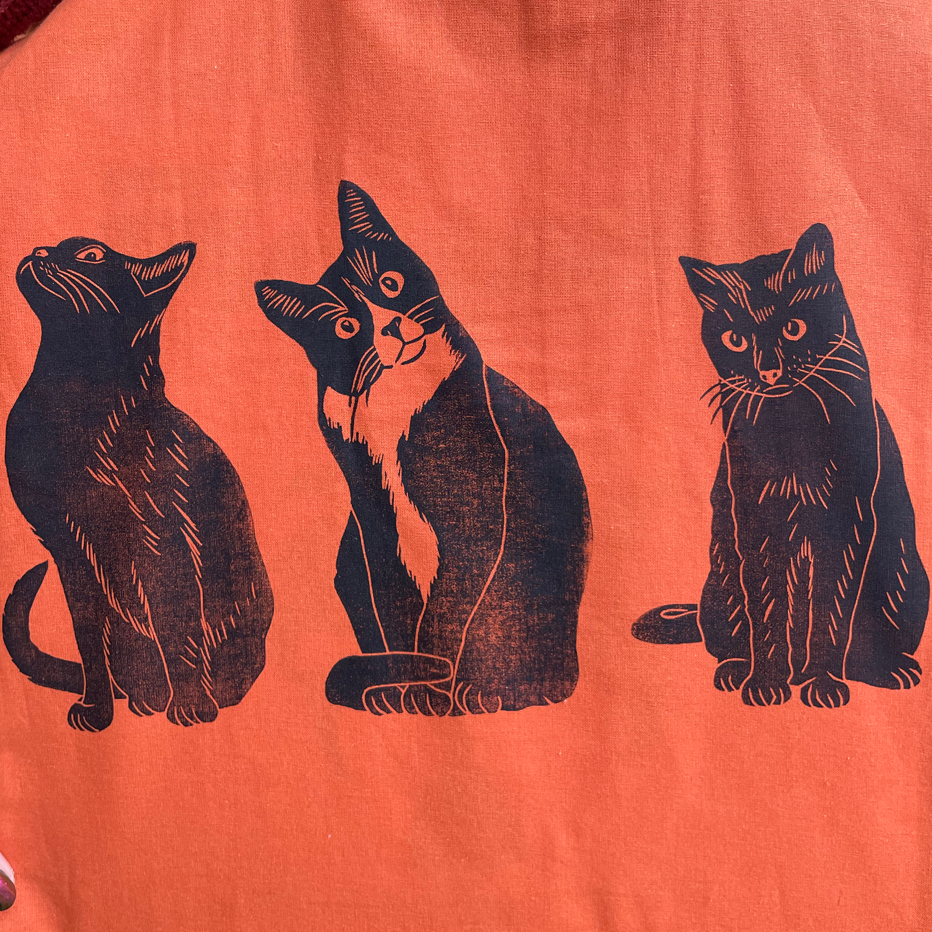 Orange tote bag with black cat illustrations held by a person.