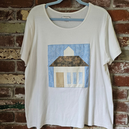 White sleeveless top with blue & cream house quilt patch design on a brick wall background