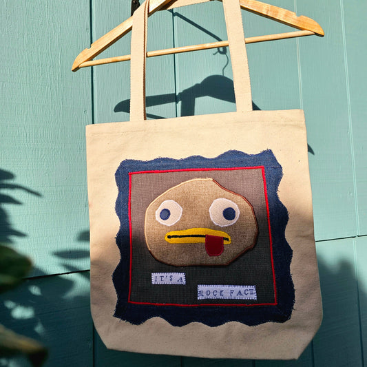 Tote bag with rock fact design from Over the Garden Wall on a wooden hanger against a teal wall.