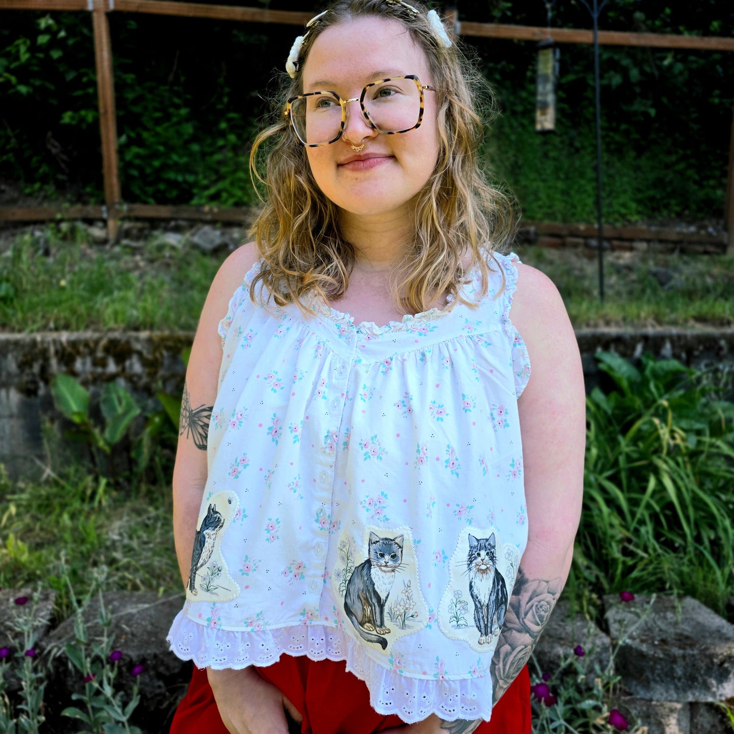 Person wearing a white blouse with cat prints and red pants standing outdoors.