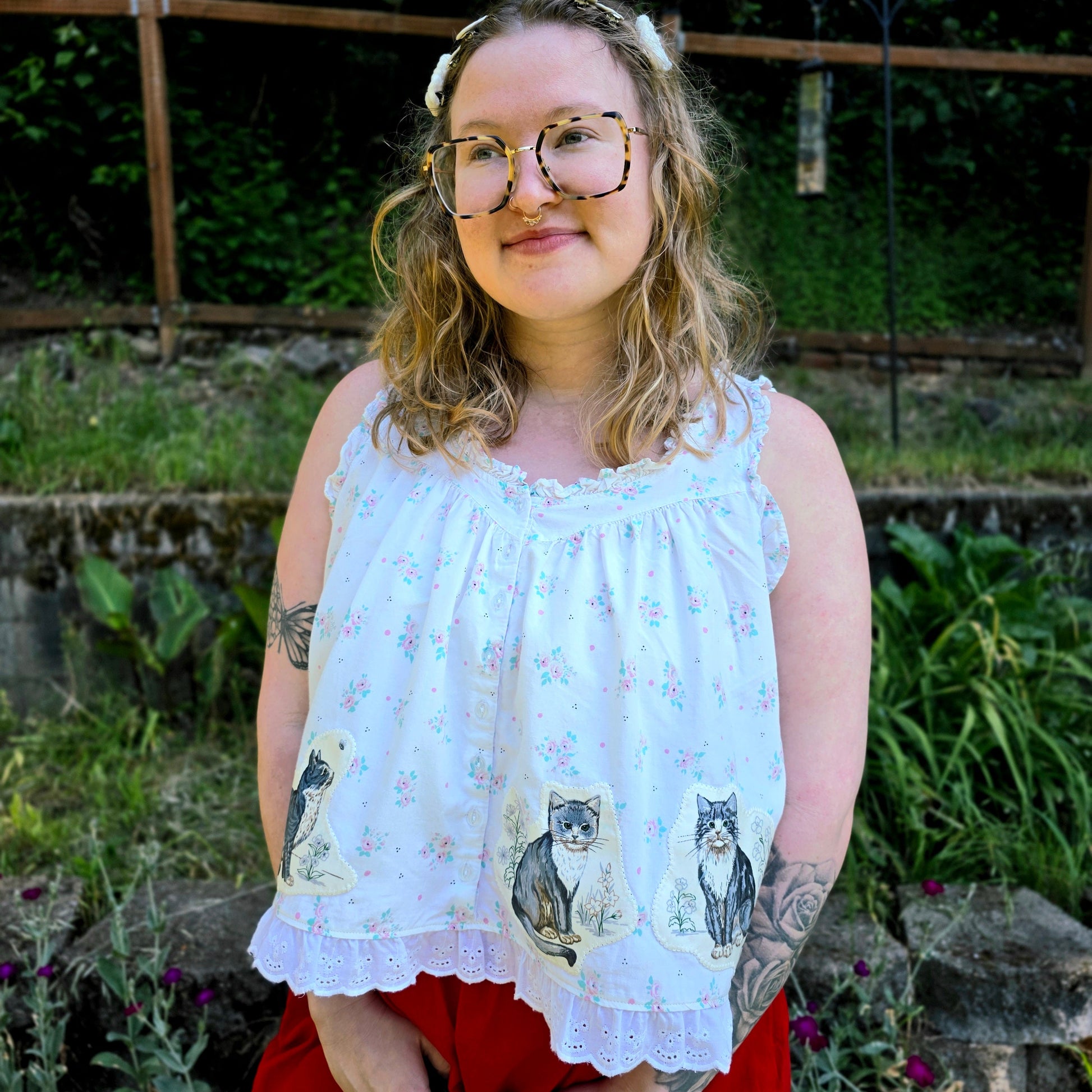 Person wearing a white blouse with cat prints and red pants standing outdoors.