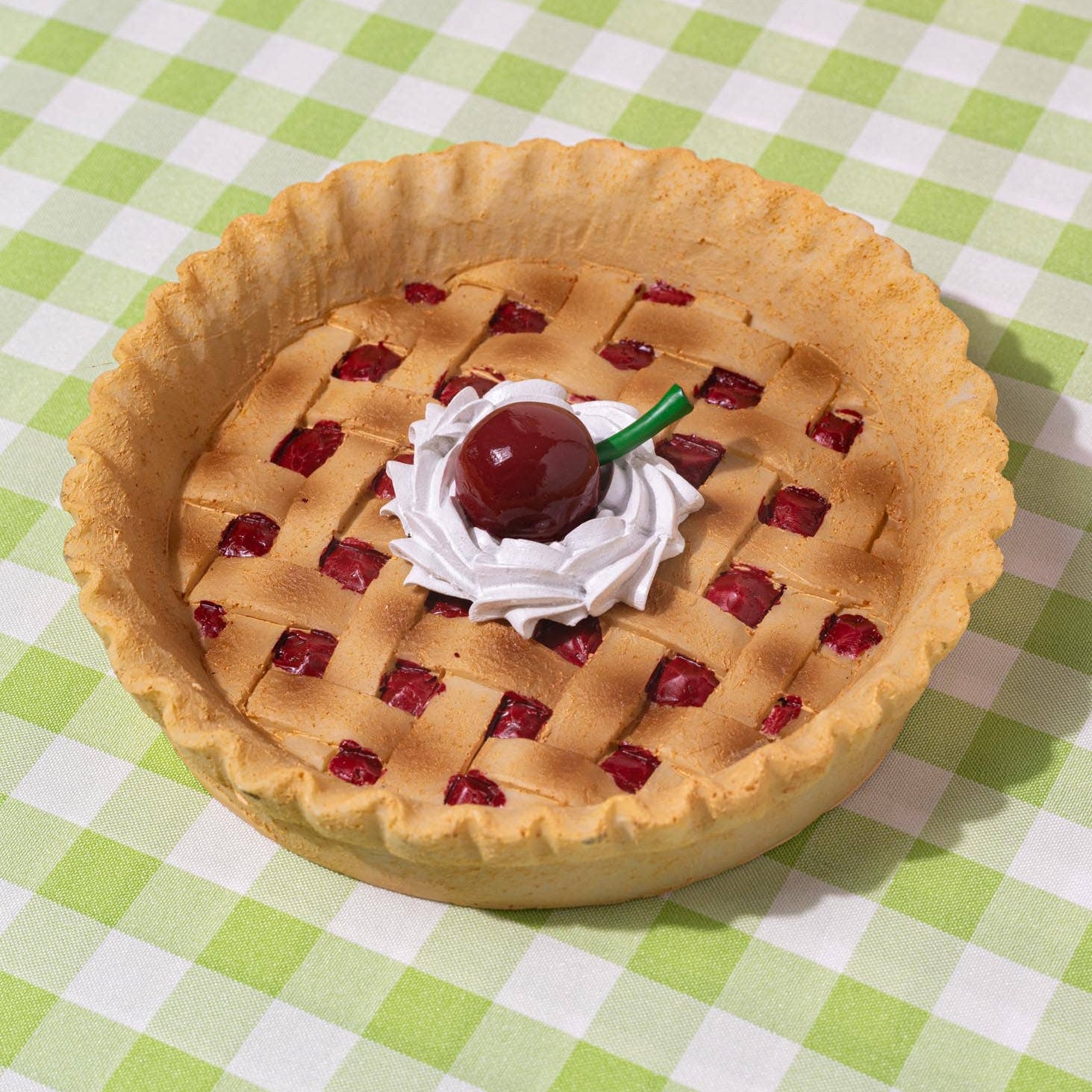 Cherry pie ashtray with whipped cream & cherry on top, on a green and white checkered tablecloth