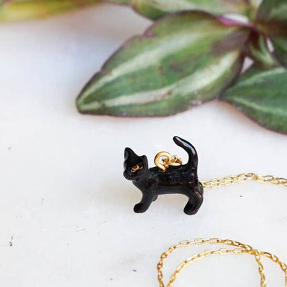 Black cat-shaped pendant on a gold chain with green leaves in the background