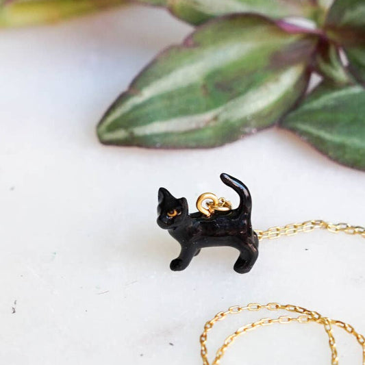 Black cat-shaped pendant on a gold chain with green leaves in the background