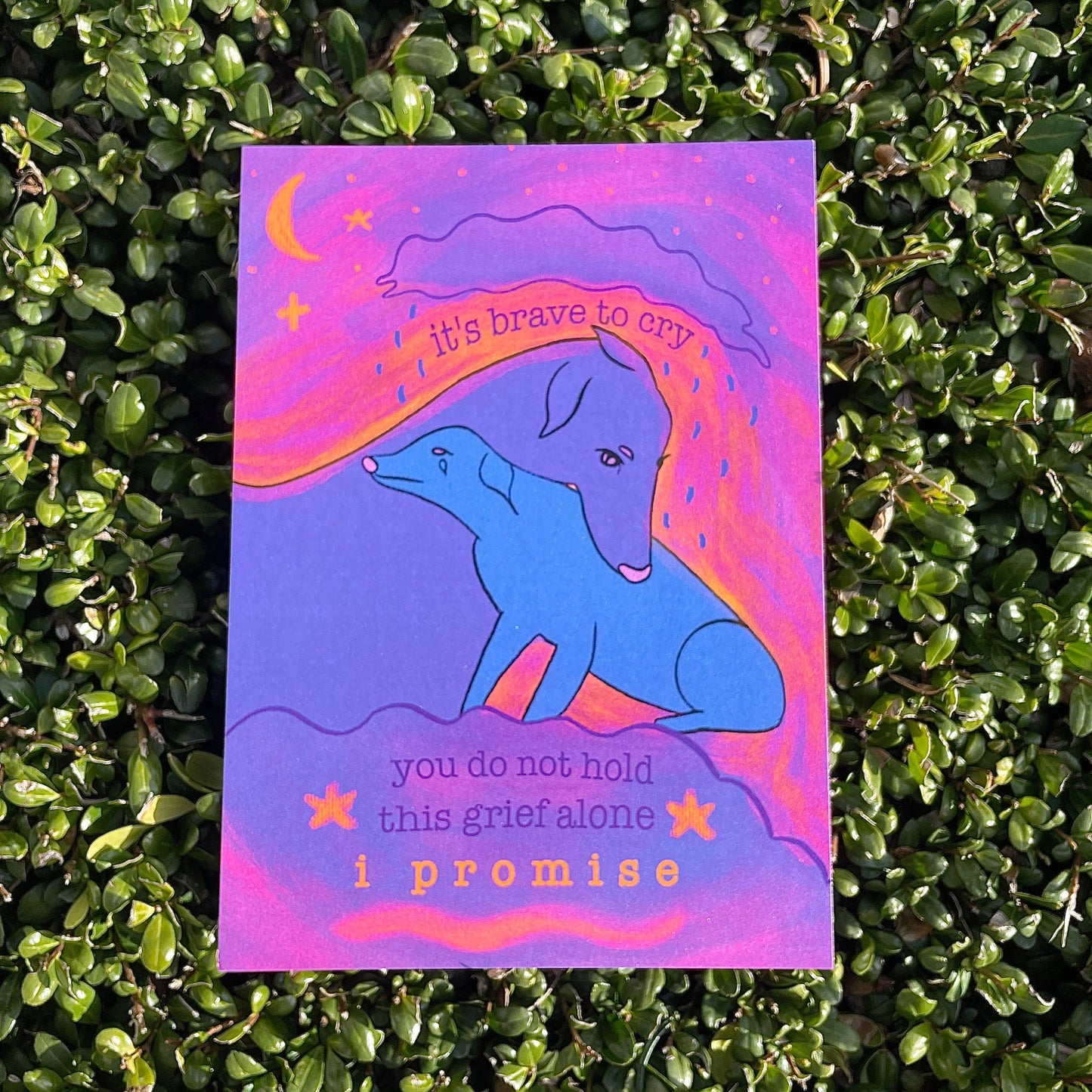 Card with a blue dog illustration and text that reads "It's brave to cry. You do not hold this grief alone. I promise" on a green foliage background