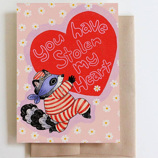 Greeting card with raccoon illustration and 'You have stolen my heart' text on a pink floral card background.