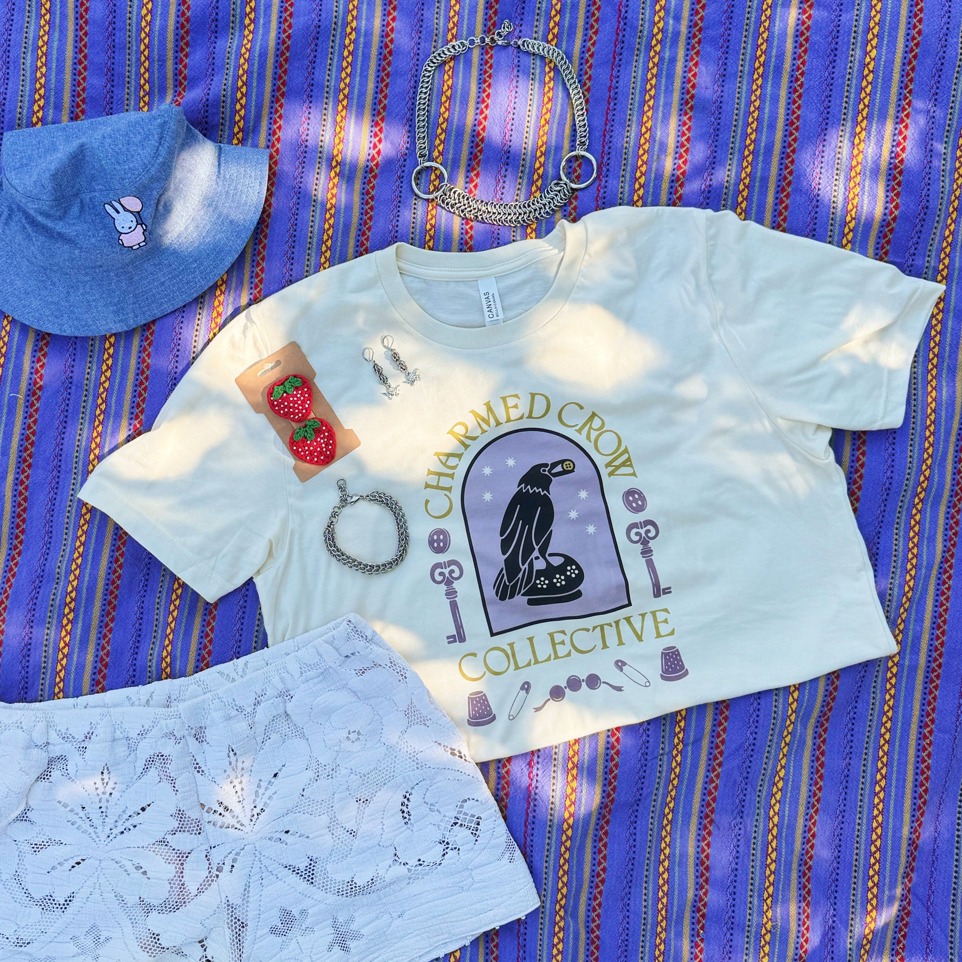 Light blue t-shirt, shorts, and hat on a striped purple blanket outdoors