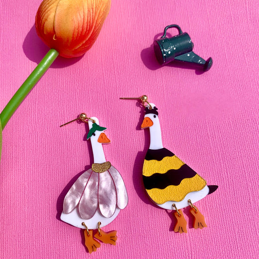Colorful goose-shaped earrings on a pink background with a tulip and watering can.