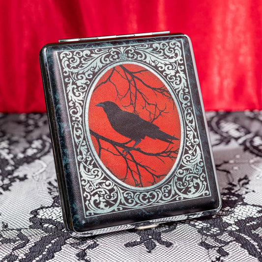 Decorative cigarette case with a crow design on a red background, placed on a lace surface.