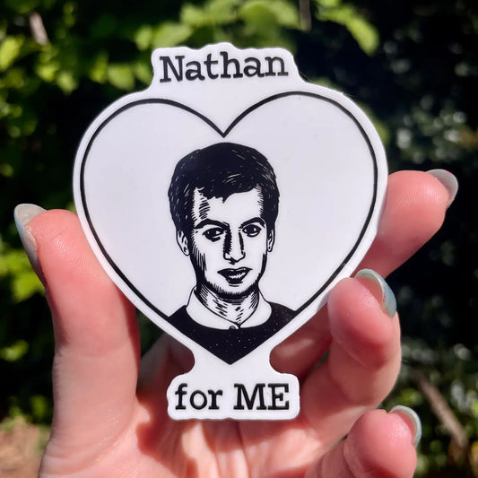 Heart-shaped sticker with a portrait and 'Nathan for ME' text held in a hand against a blurred green background