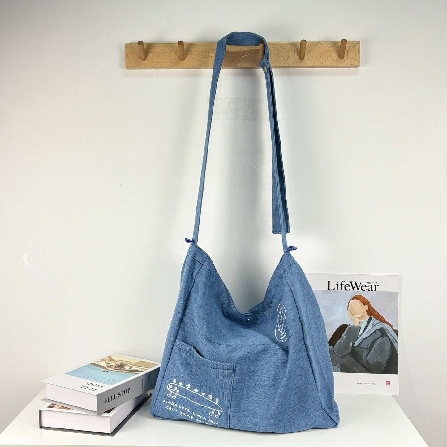 Blue shoulder bag hanging on a wooden rack with books and a magazine below.