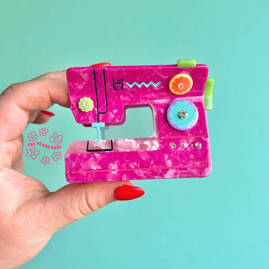 Pink sewing machine hair claw held in a hand against a teal background