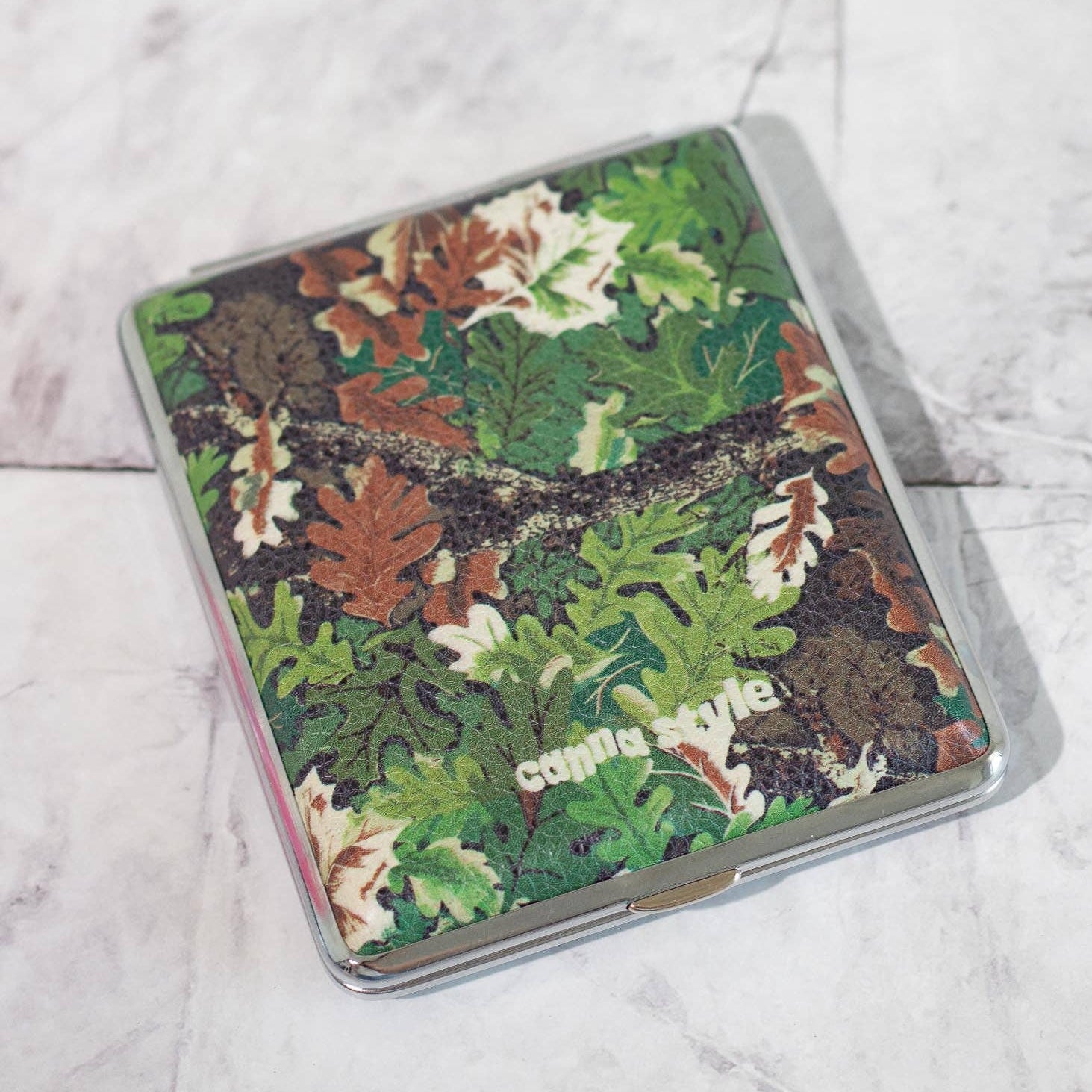 Camouflage-patterned cigarette case with 'Canna Style' branding on a marble surface