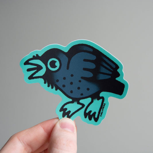 Hand holding a blue and black crow-shaped sticker against a gray background