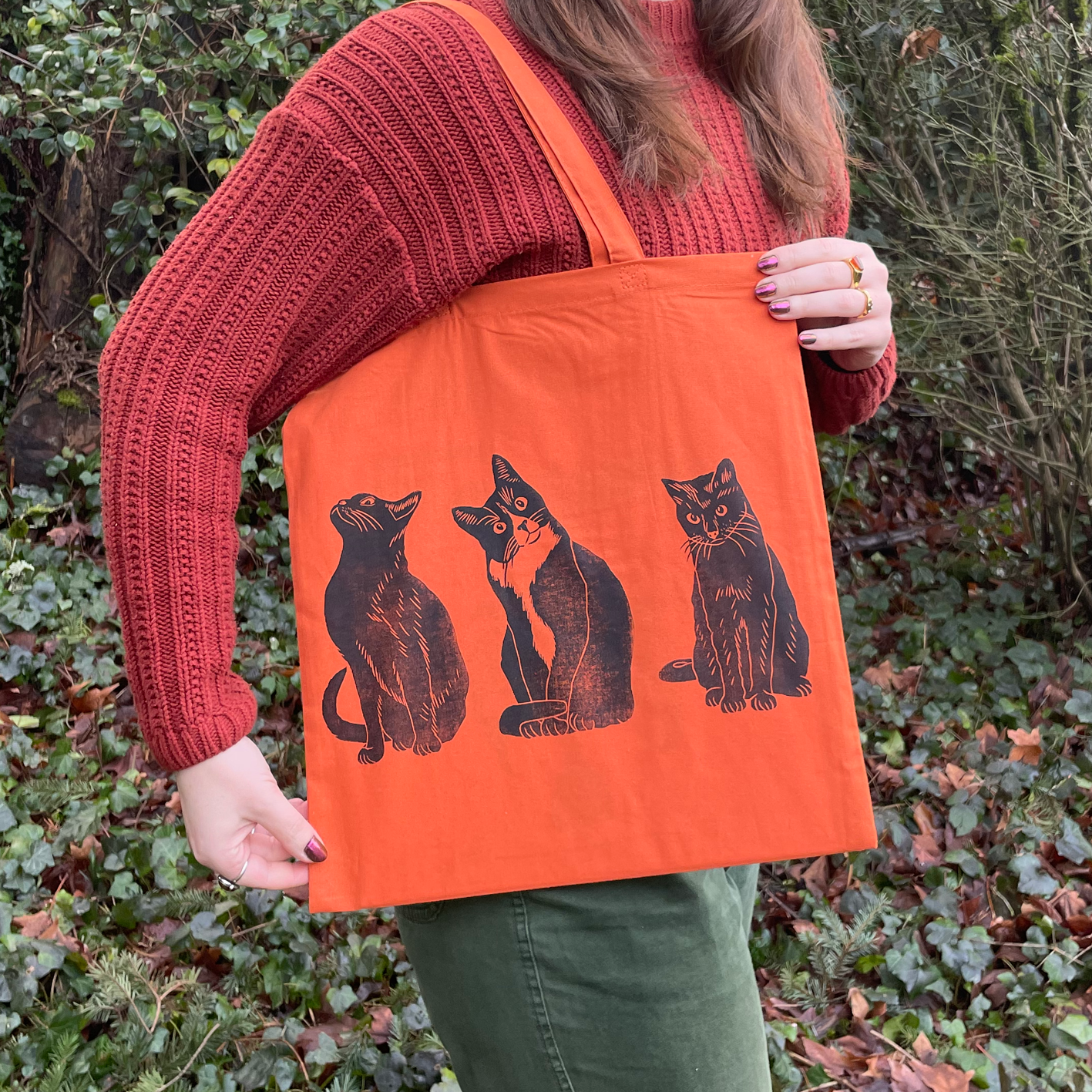 Person holding an orange tote bag with cat design outdoors