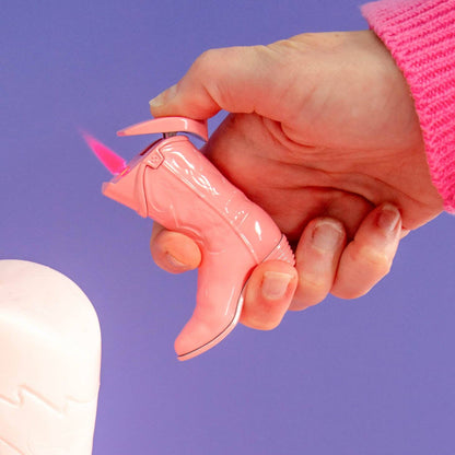 Hand holding a pink cowboy boot shaped lighter against a purple background