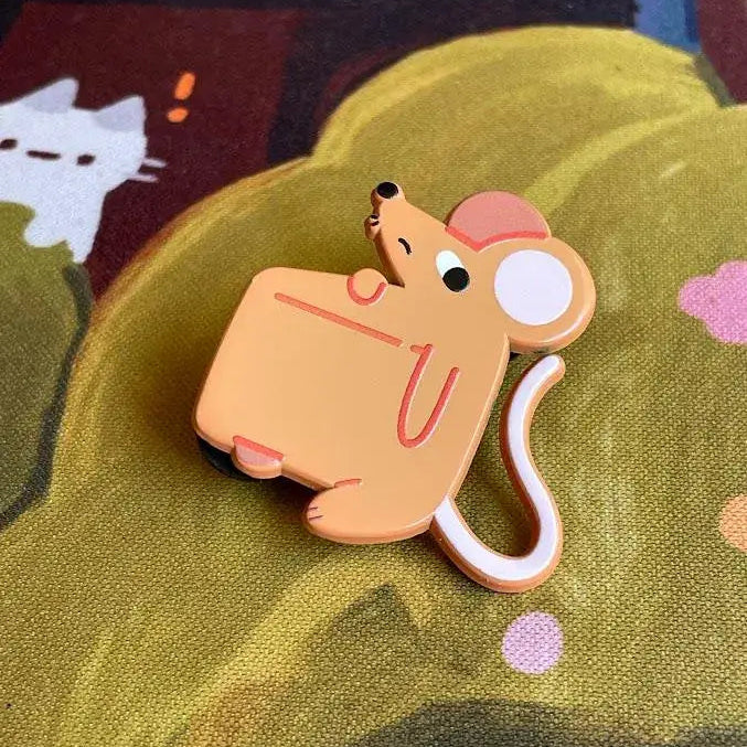 Cartoon mouse character pin full of a cheese wedge on a textured green surface