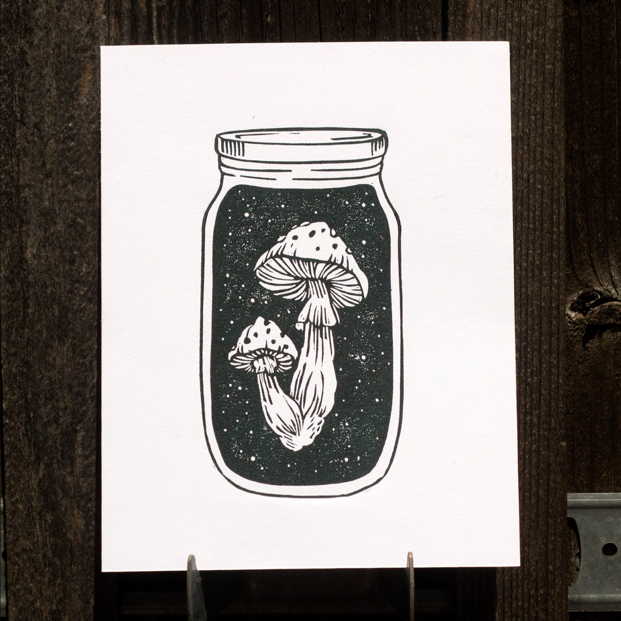 Linocut print of mushrooms inside a mason jar on a white background
