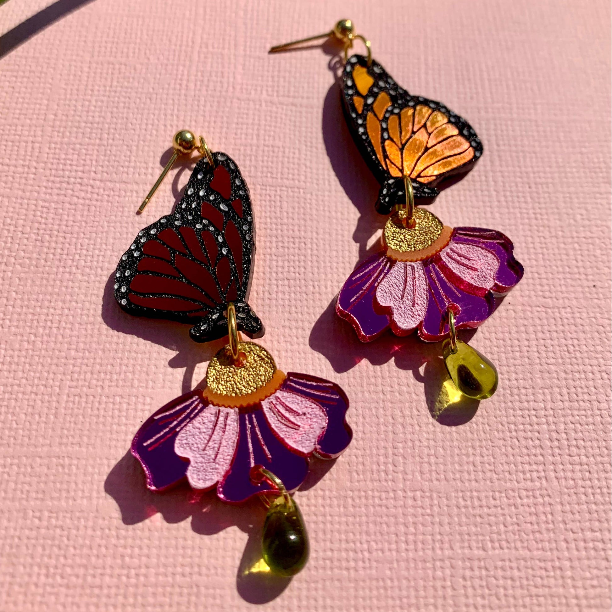 Monarch butterfly and purple flower earrings on a pink background
