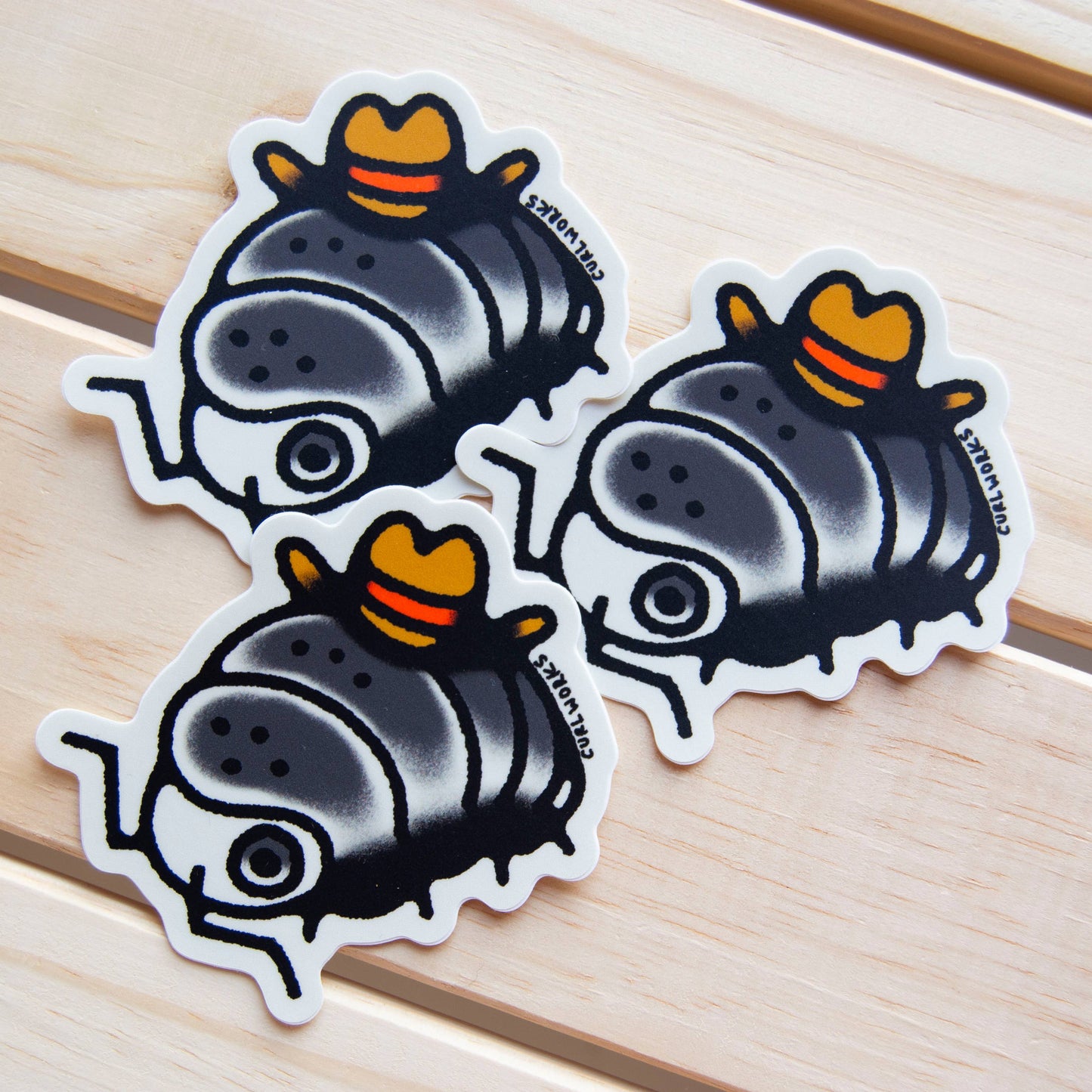 Three cartoonish pillbug wearing cowboy hat stickers on a wooden surface