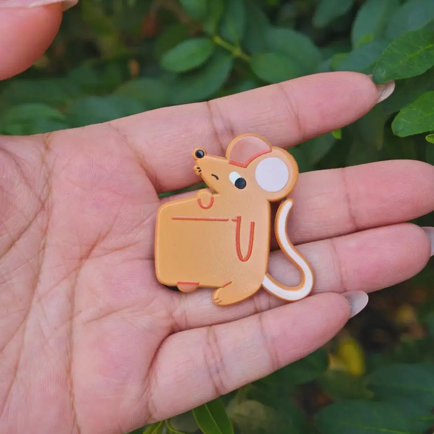 Hand holding a cartoon mouse-shaped object with a green leafy background