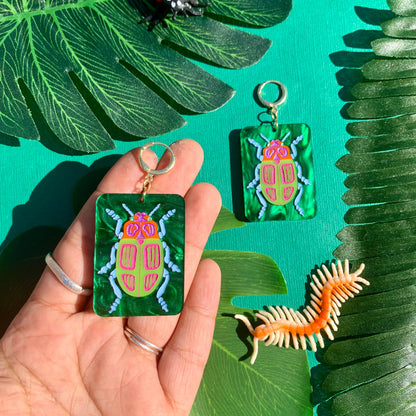 Hand holding earrings with a beetle design on a green leaf background