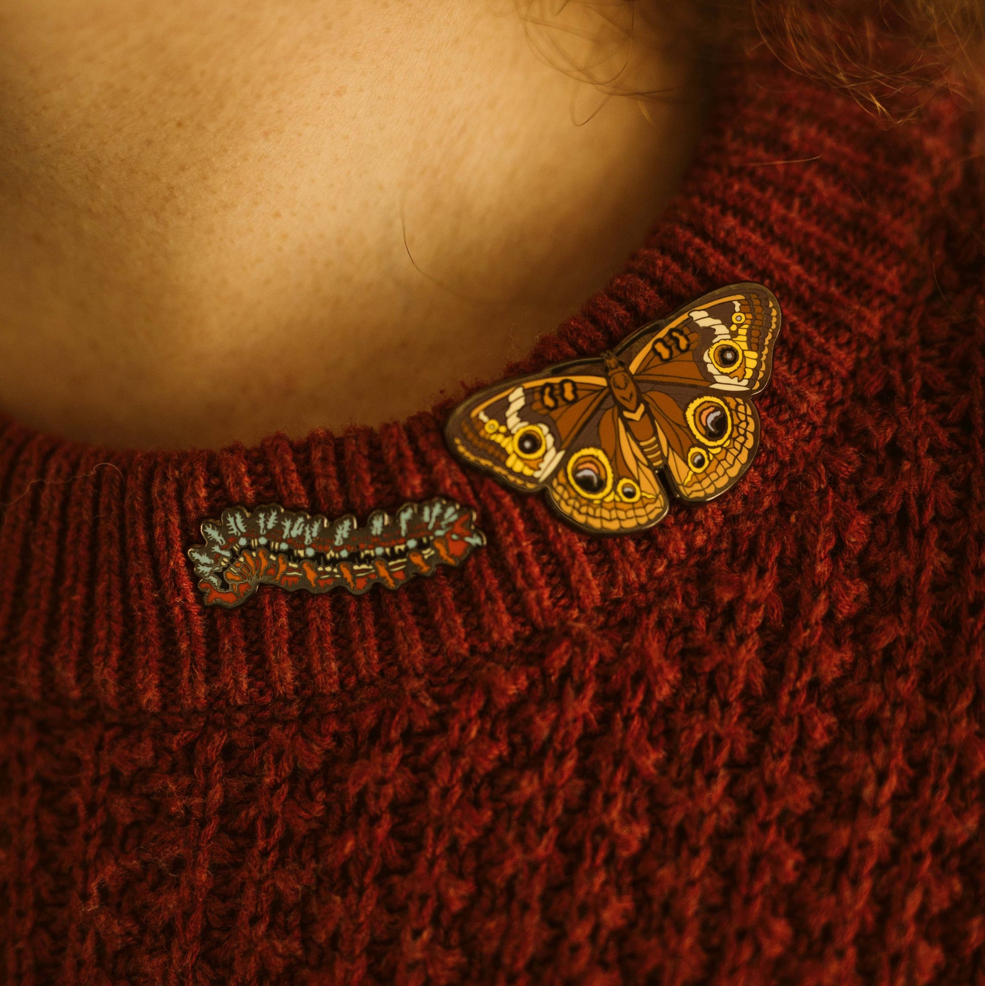 Close-up of a red sweater with butterfly and caterpillar brooches.