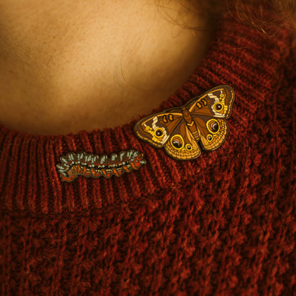 Close-up of a red sweater with butterfly and caterpillar brooches.