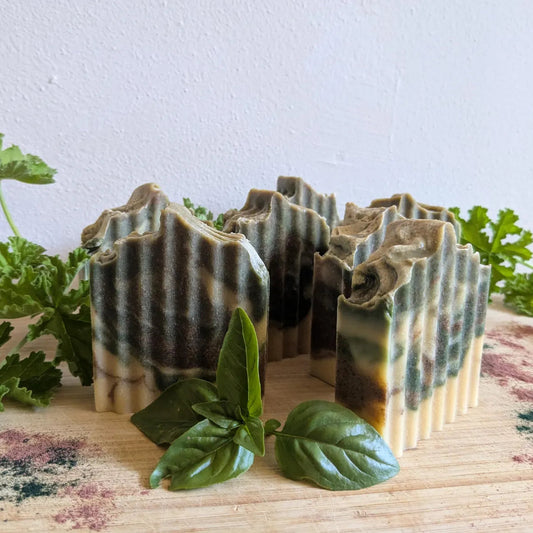 Three bars of soap with a natural, earthy pattern on a wooden surface with green leaves.