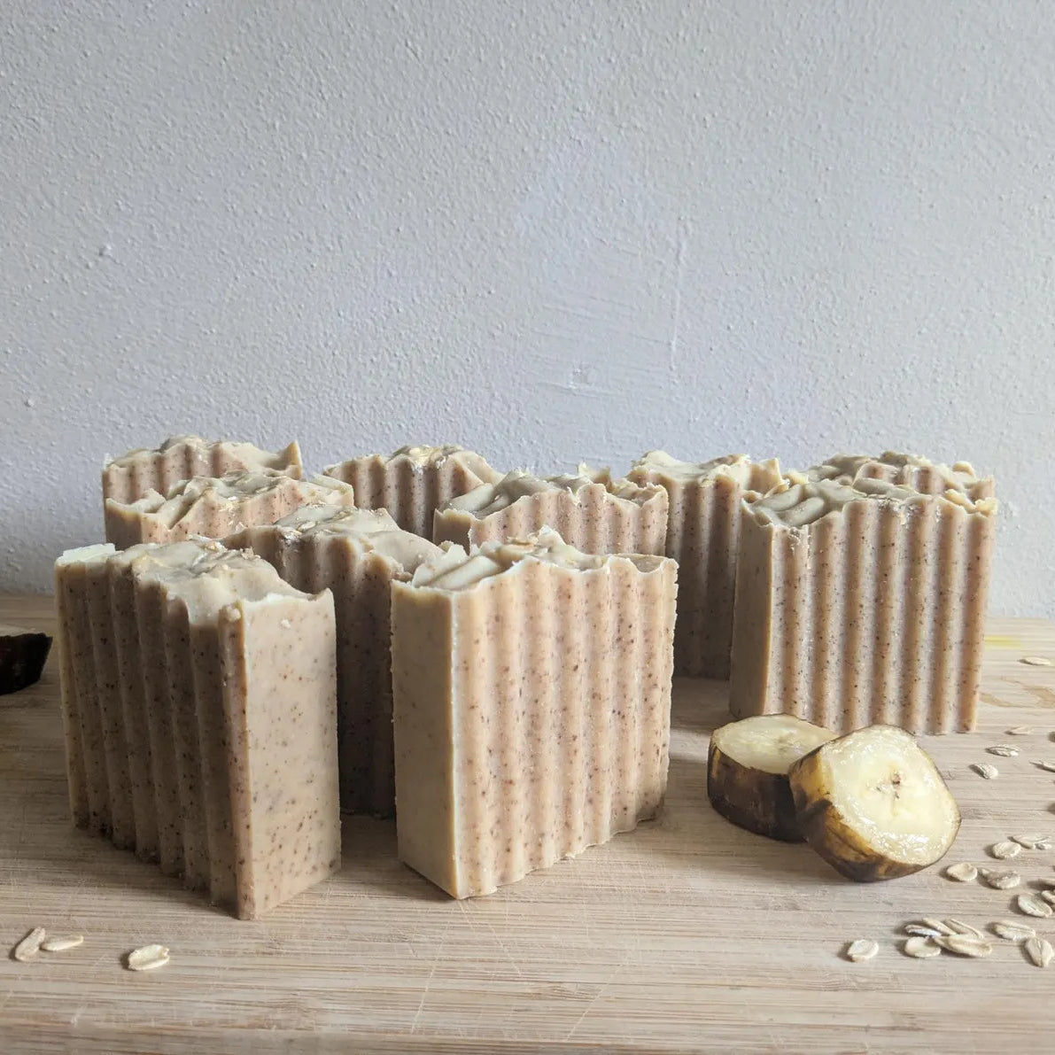 Bar soaps with a textured surface on a wooden board with oats and a banana.
