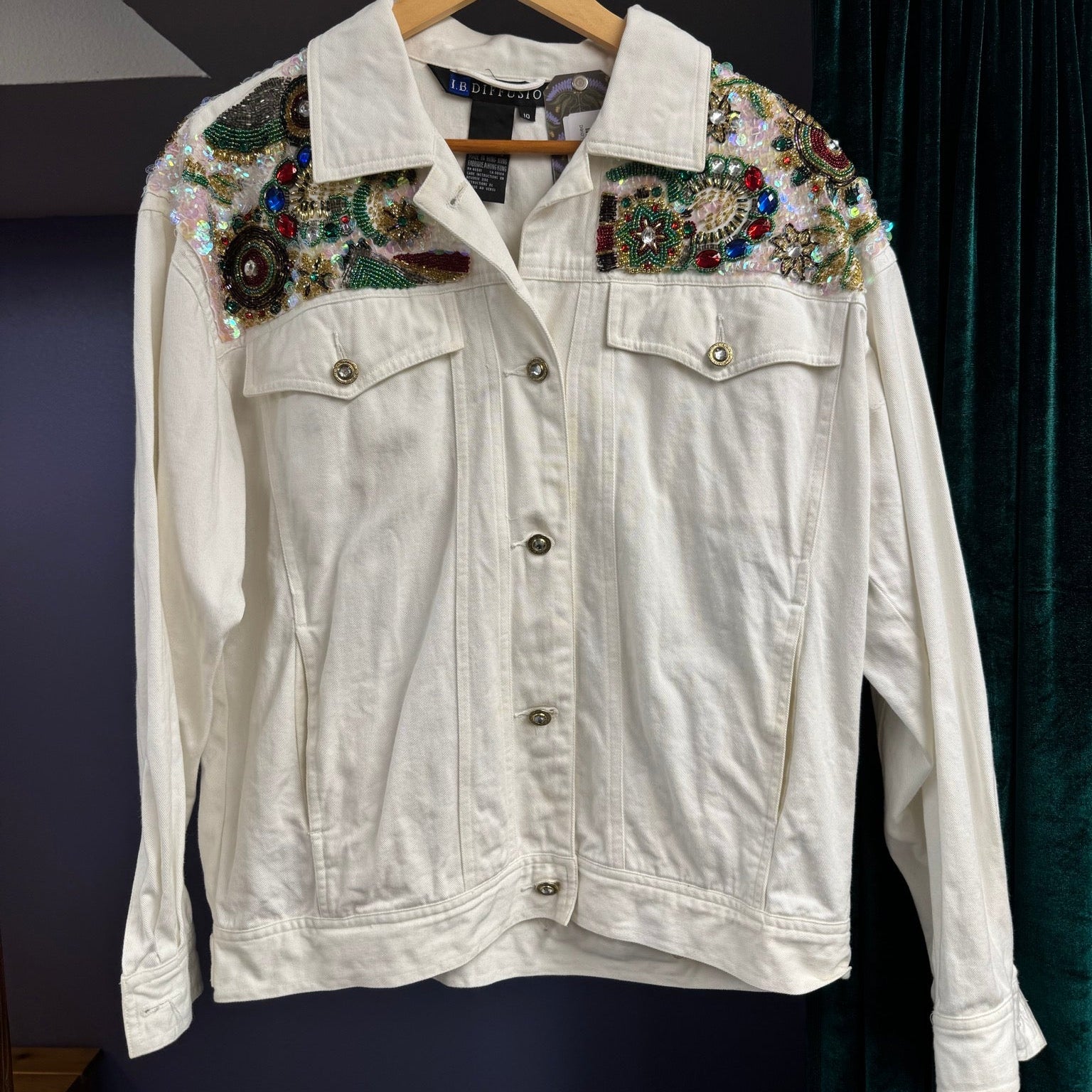 White denim jacket with embellishments on a hanger against a dark background